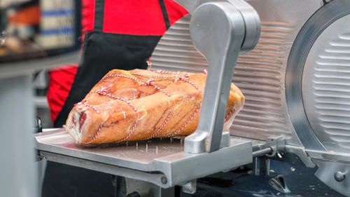 Chef slicing ham on a commercial meat slicer